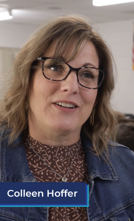 A middle aged white woman with blonde hair and glasses stands in a classroom. She wears a dark orange top and a jean jacket. In the bottom left corner is a blue box with white text in it that reads "Colleen Hoffer". Michigan Special Education Teacher