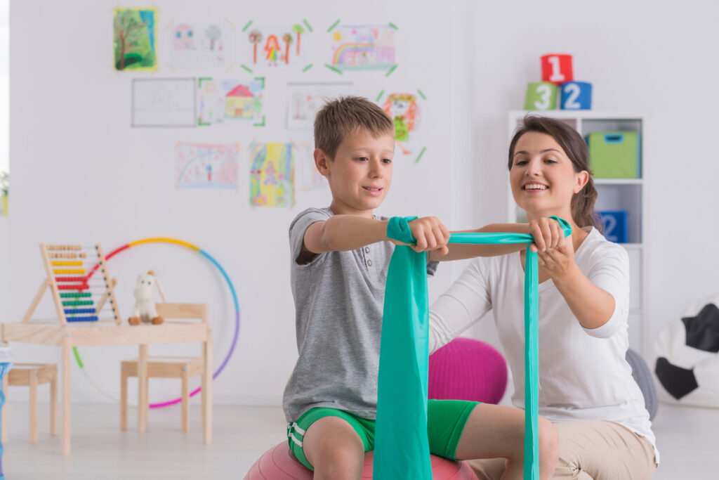 Physical therapist helping a young boy exercise with a resistance band during a therapy session.