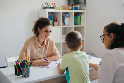 School psychologist sitting at a desk with a young child and parent, discussing emotional and educational support.