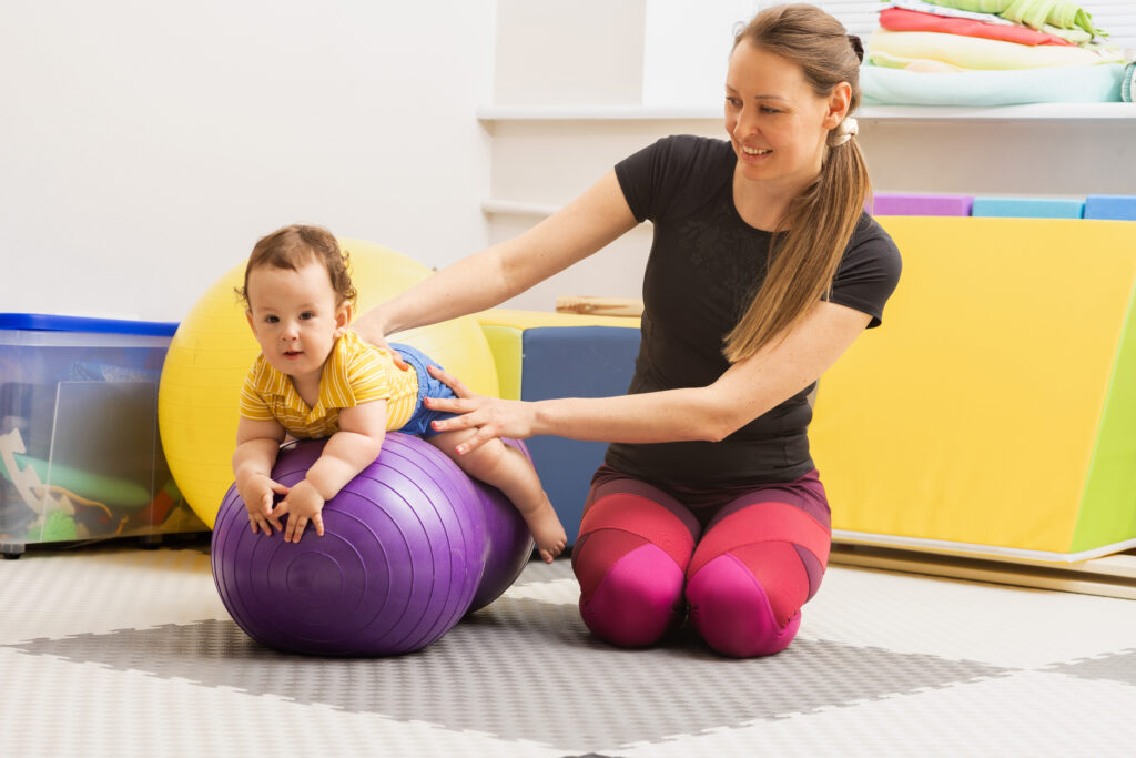 Early intervention specialist helping a baby with motor skills using a therapy ball in a colorful setting.