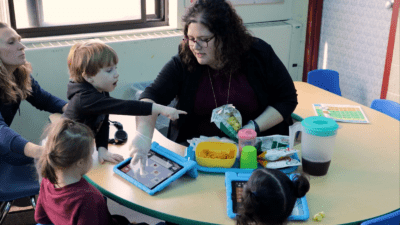 Teacher guiding young children with disabilities using tablets for communication