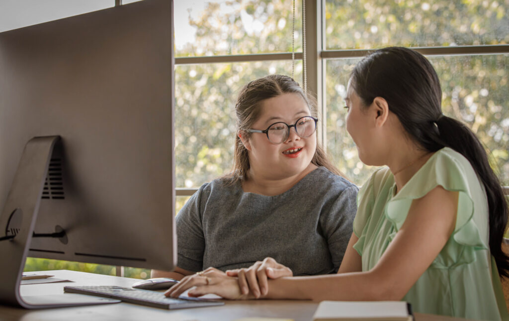 Student with Down syndrome engaging in a positive conversation with a peer at a computer workstation